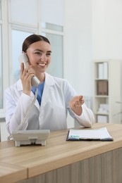 Photo of Professional receptionist talking on phone at wooden desk in hospital