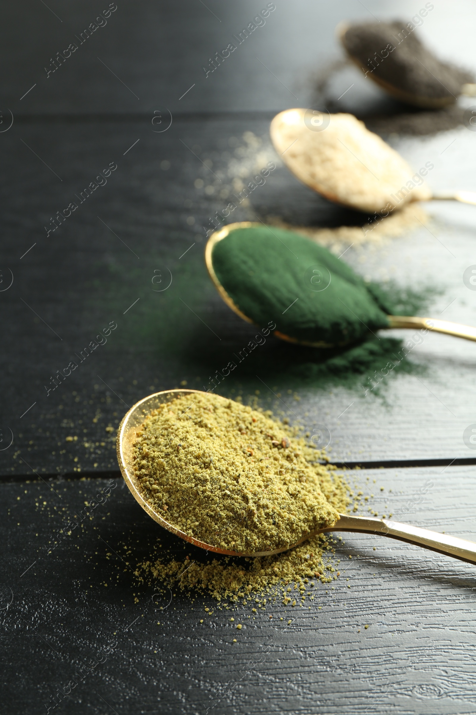 Photo of Different superfood powders in spoons on black wooden table, closeup