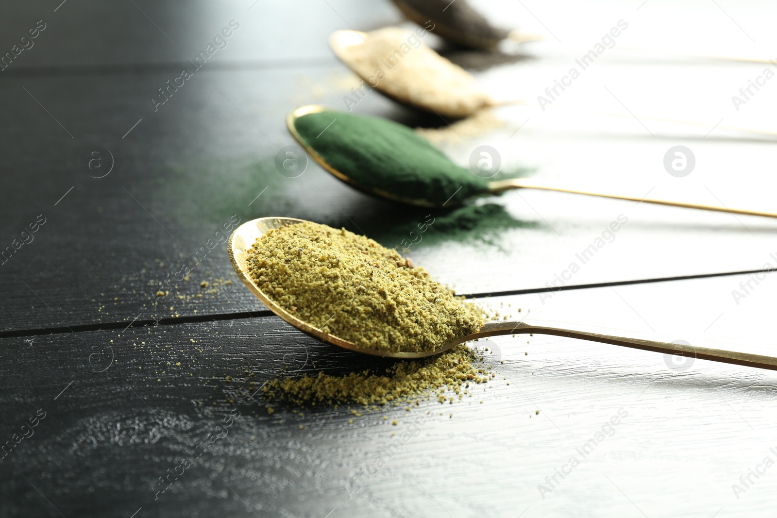 Photo of Different superfood powders in spoons on black wooden table, closeup