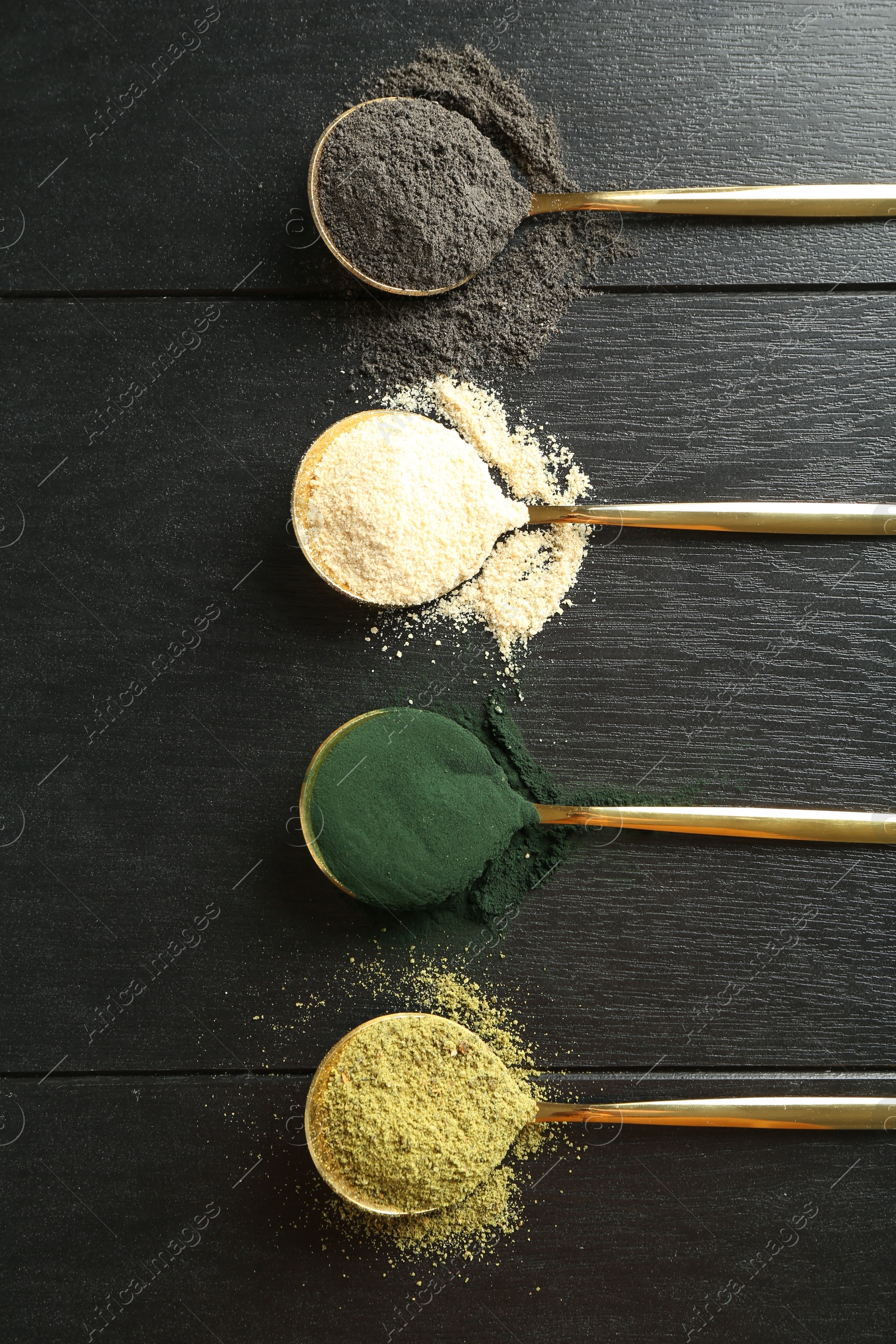 Photo of Different superfood powders in spoons on black wooden table, flat lay