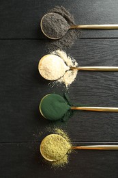 Different superfood powders in spoons on black wooden table, flat lay