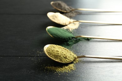 Different superfood powders in spoons on black wooden table, closeup