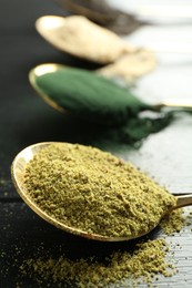 Photo of Different superfood powders in spoons on black wooden table, closeup