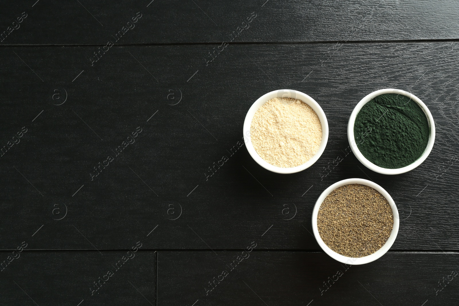 Photo of Different healthy superfoods in bowls on black wooden table, flat lay. Space for text