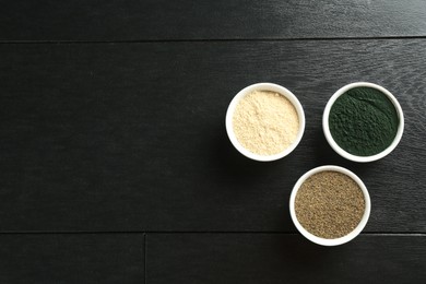 Different healthy superfoods in bowls on black wooden table, flat lay. Space for text