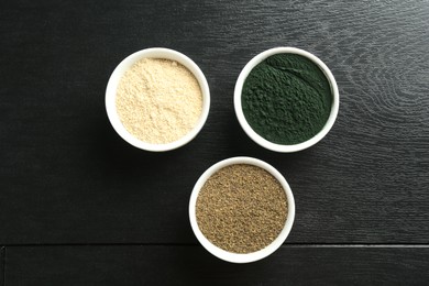 Photo of Different healthy superfoods in bowls on black wooden table, flat lay