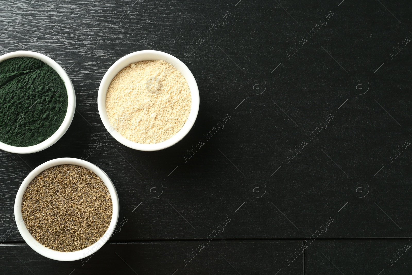 Photo of Different healthy superfoods in bowls on black wooden table, flat lay. Space for text