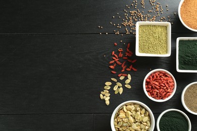 Photo of Different healthy superfoods in bowls on black wooden table, flat lay. Space for text