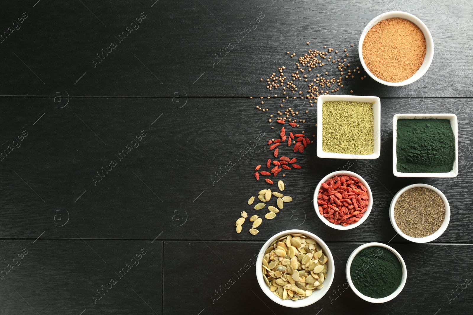 Photo of Different healthy superfoods in bowls on black wooden table, flat lay. Space for text