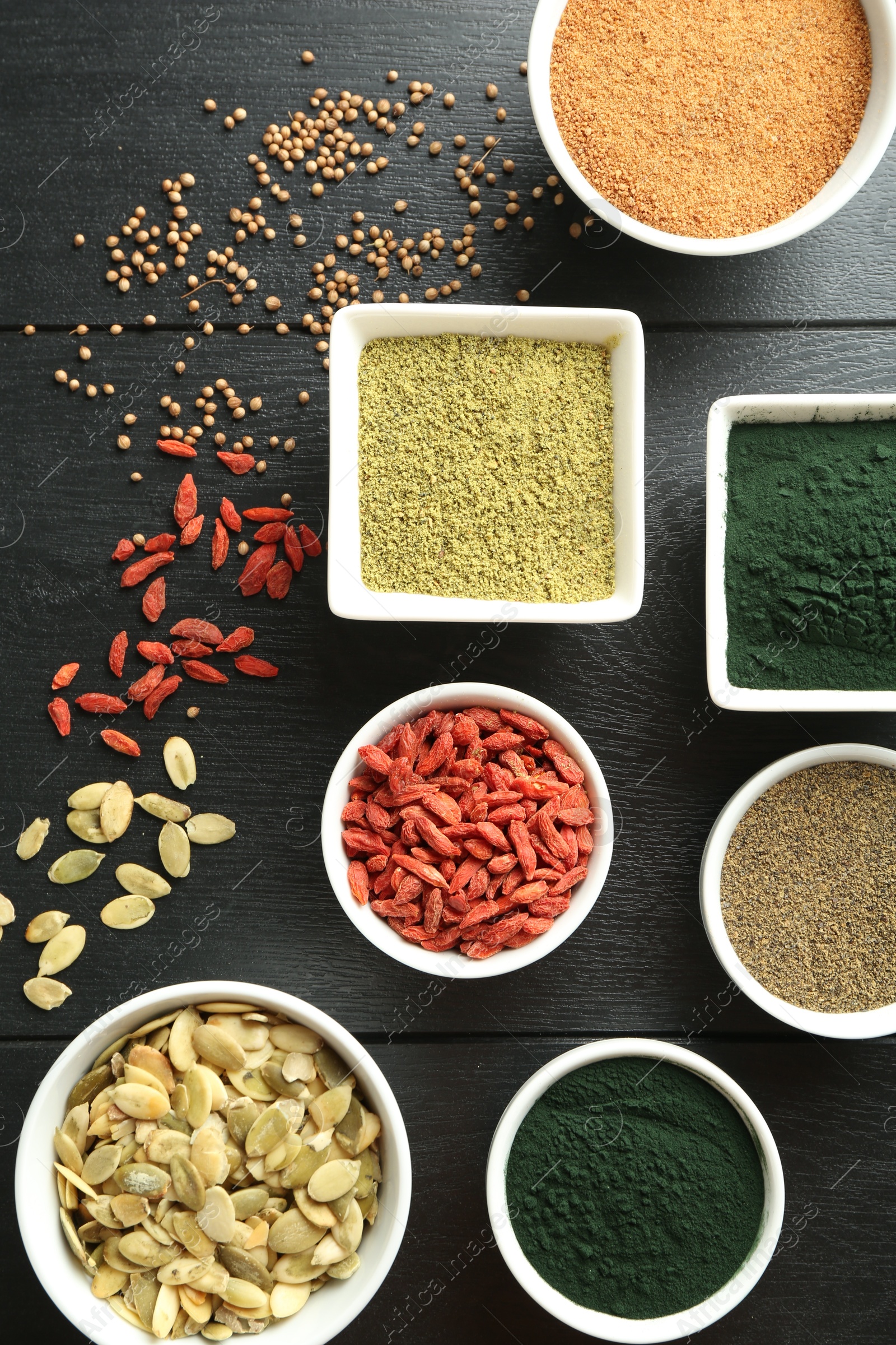 Photo of Different healthy superfoods in bowls on black wooden table, flat lay