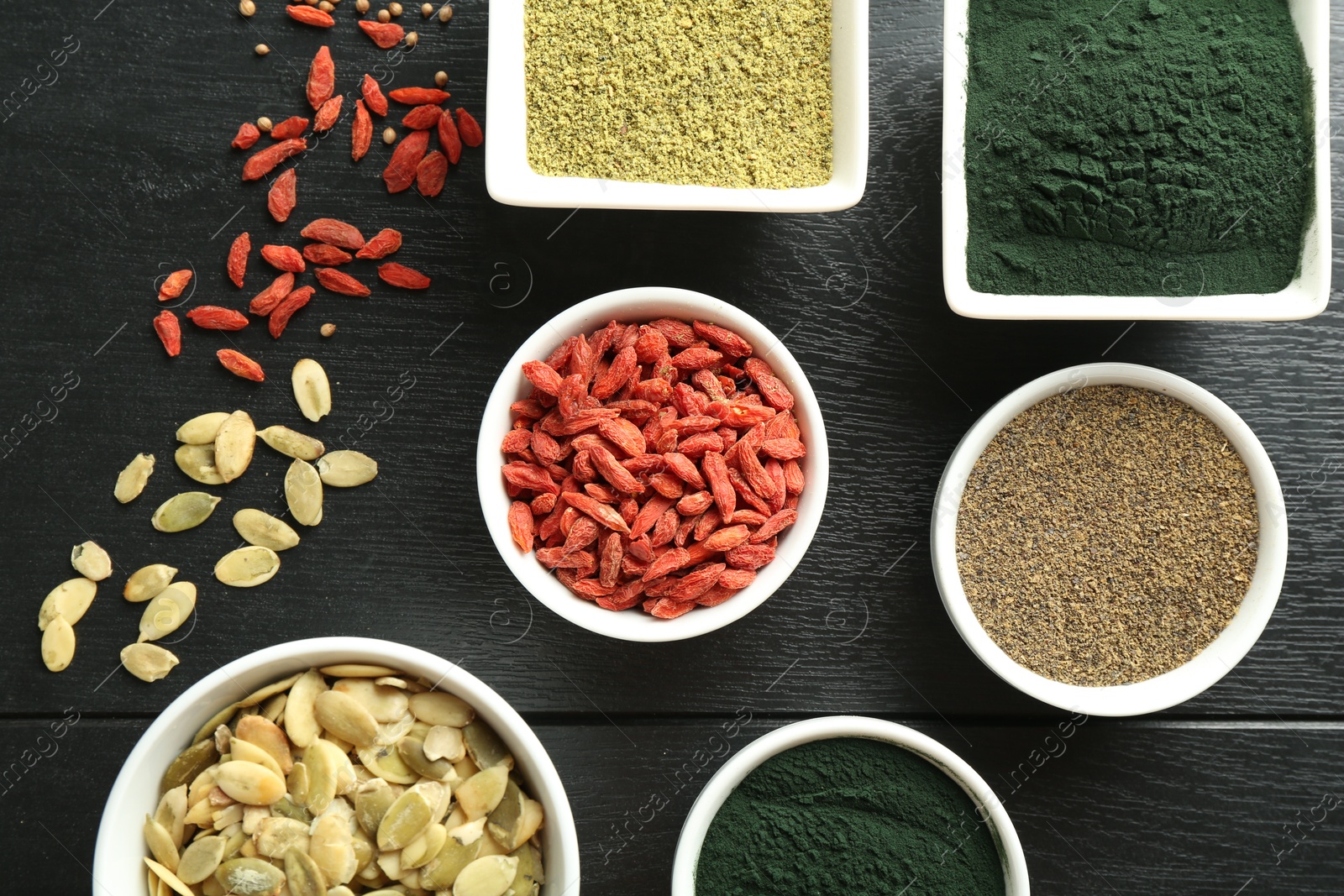 Photo of Different healthy superfoods in bowls on black wooden table, flat lay