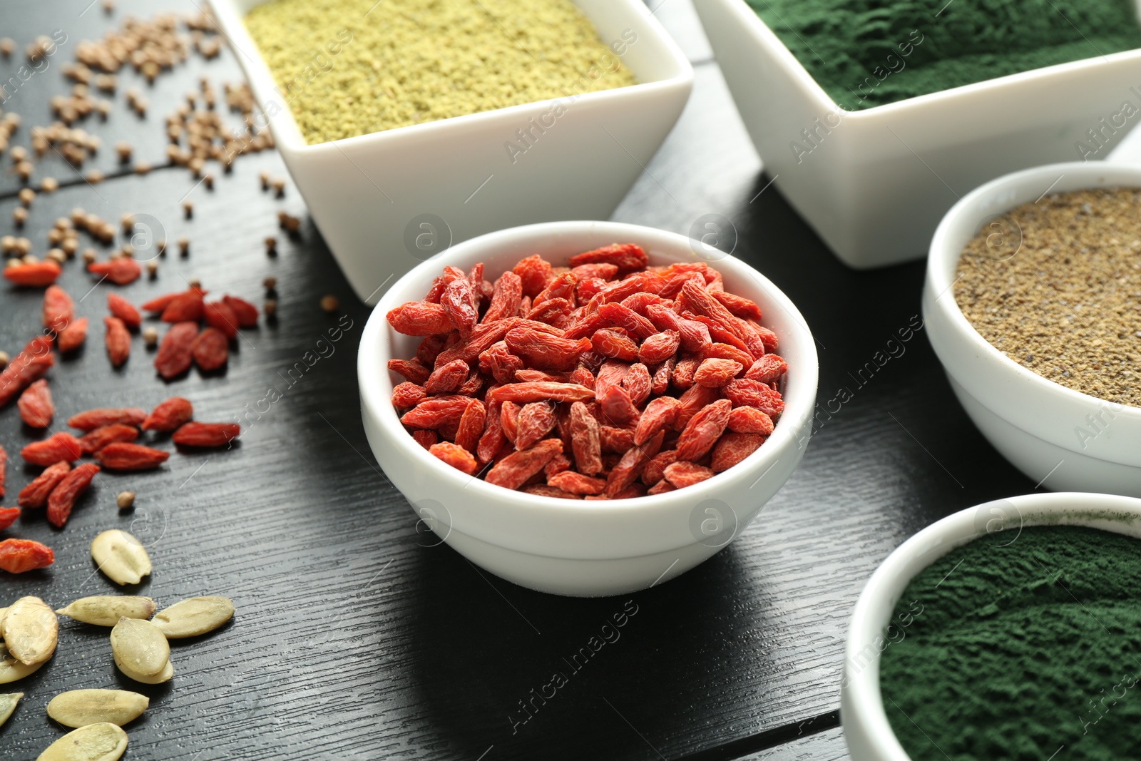 Photo of Different healthy superfoods in bowls on black wooden table, closeup