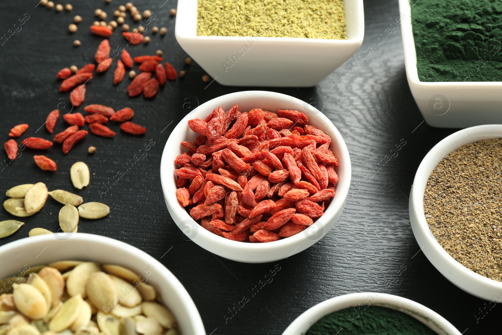 Photo of Different healthy superfoods in bowls on black wooden table, closeup