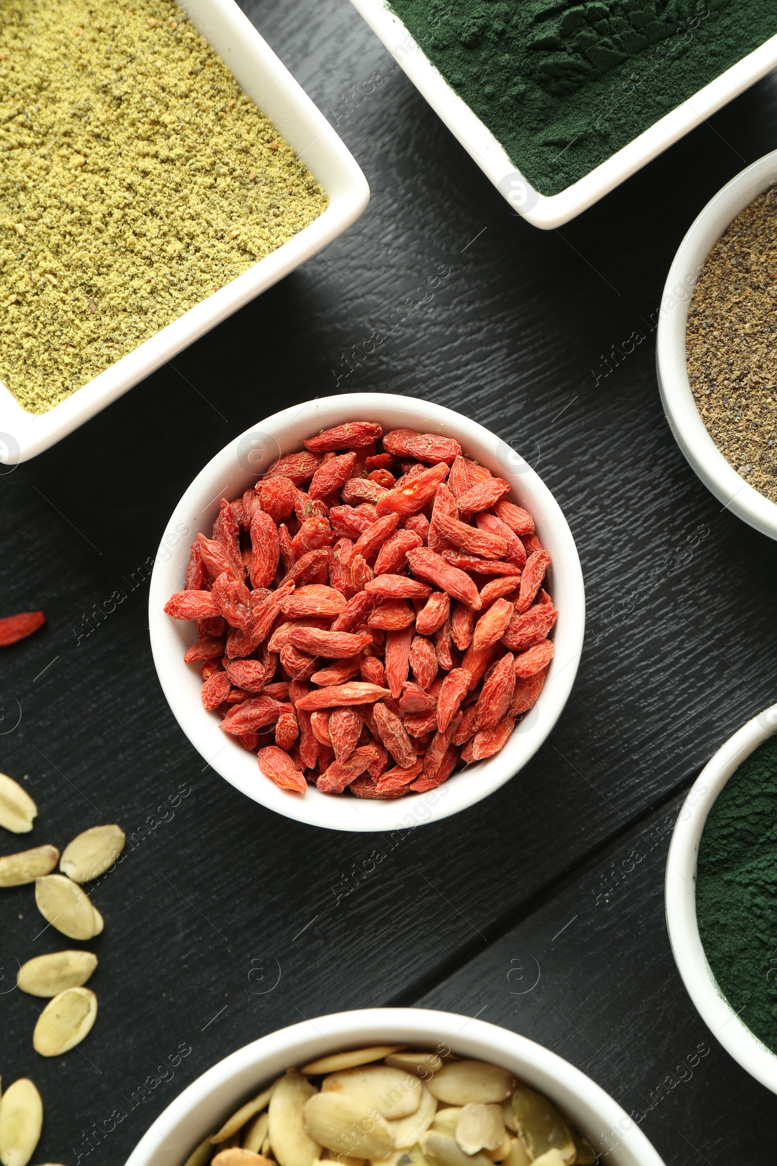 Photo of Different healthy superfoods in bowls on black wooden table, flat lay