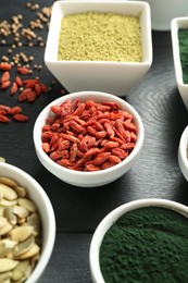 Photo of Different healthy superfoods in bowls on black wooden table