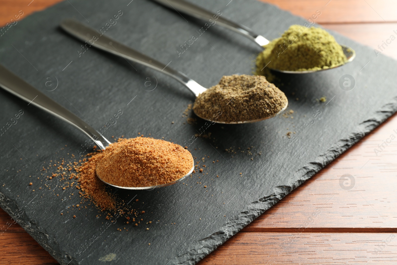 Photo of Different superfood powders in spoons on wooden table, closeup