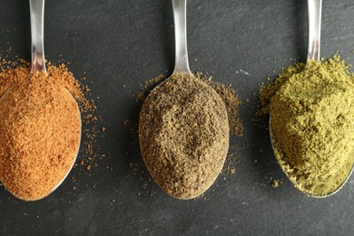 Photo of Different superfood powders in spoons on black table, flat lay