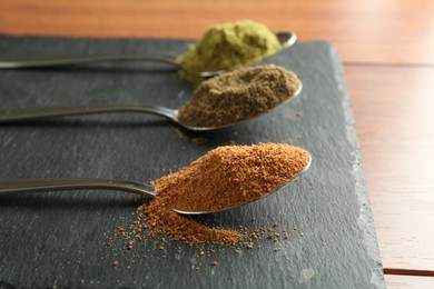 Photo of Different superfood powders in spoons on wooden table, closeup