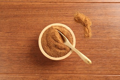 Superfood powder in bowl and spoon on wooden table, top view