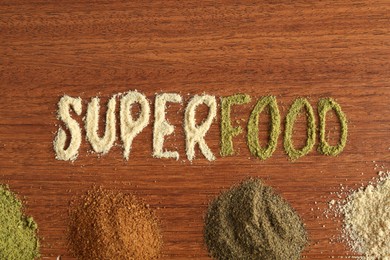 Photo of Word Superfood and different healthy powders on wooden table, flat lay