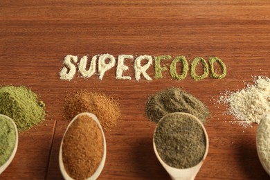 Photo of Word Superfood and different healthy powders on wooden table