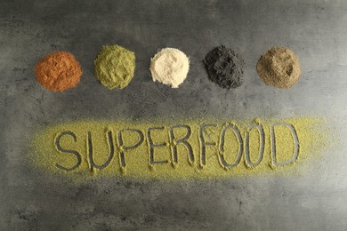 Photo of Word Superfood and different healthy powders on grey table, flat lay