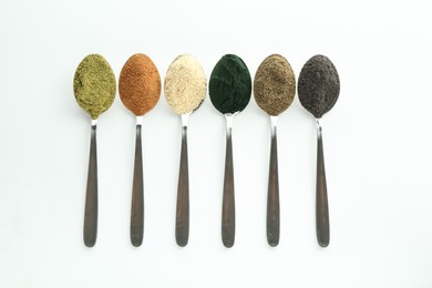 Different superfood powders in spoons on white background, flat lay