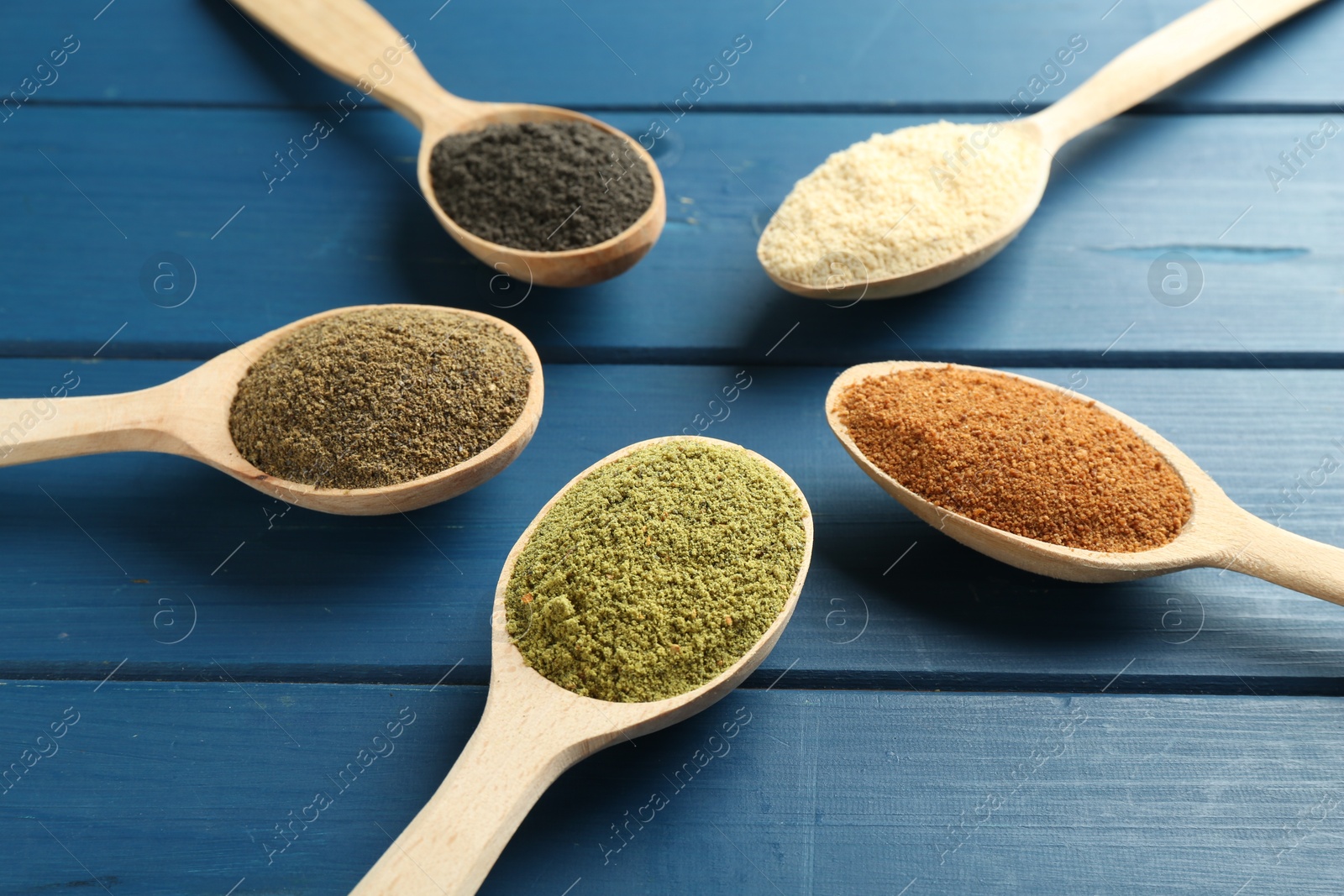 Photo of Different superfood powders in spoons on blue wooden table, closeup