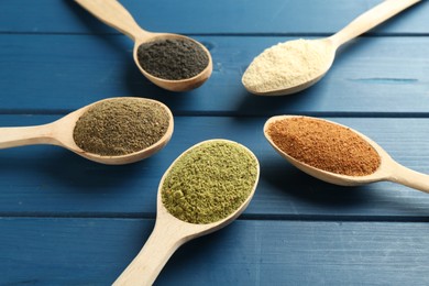 Different superfood powders in spoons on blue wooden table, closeup