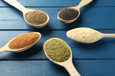 Photo of Different superfood powders in spoons on blue wooden table, closeup