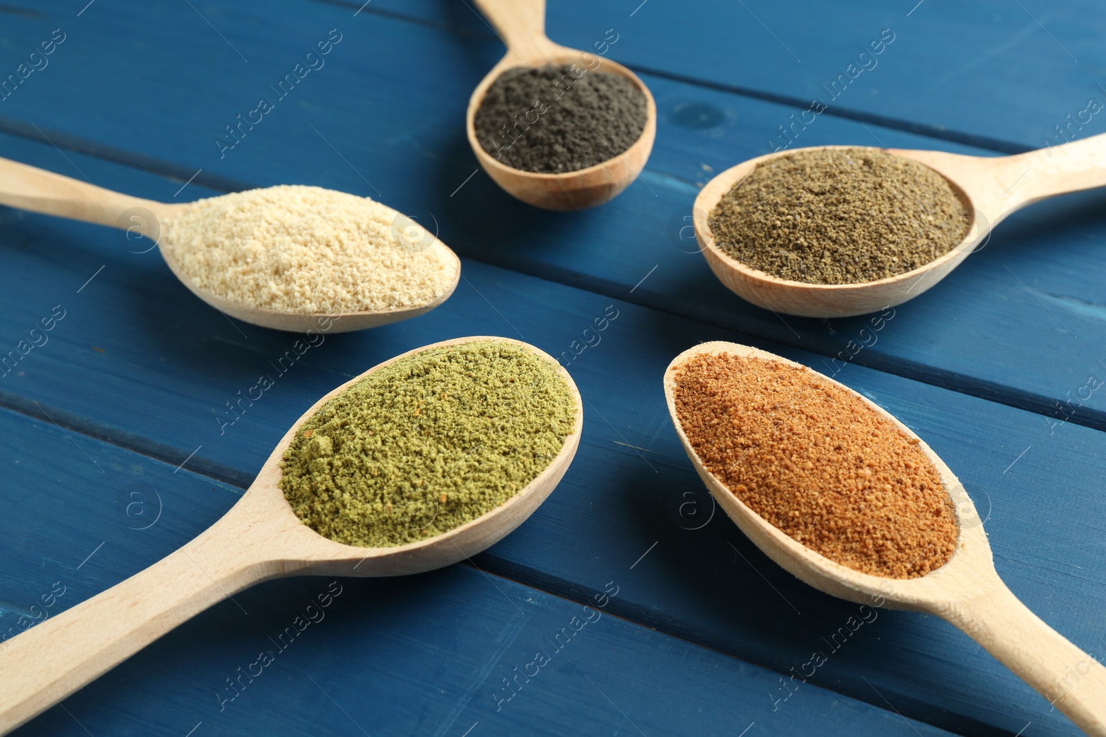 Photo of Different superfood powders in spoons on blue wooden table, closeup