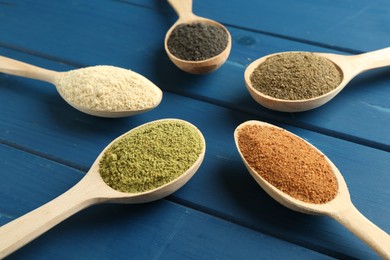 Different superfood powders in spoons on blue wooden table, closeup