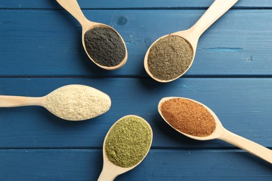 Different superfood powders in spoons on blue wooden table, above view