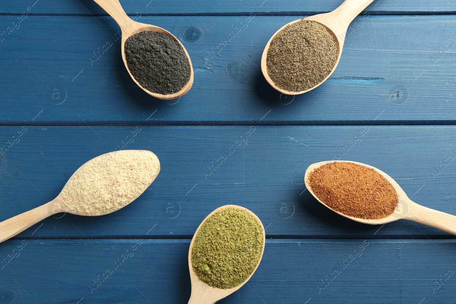 Photo of Different superfood powders in spoons on blue wooden table, above view