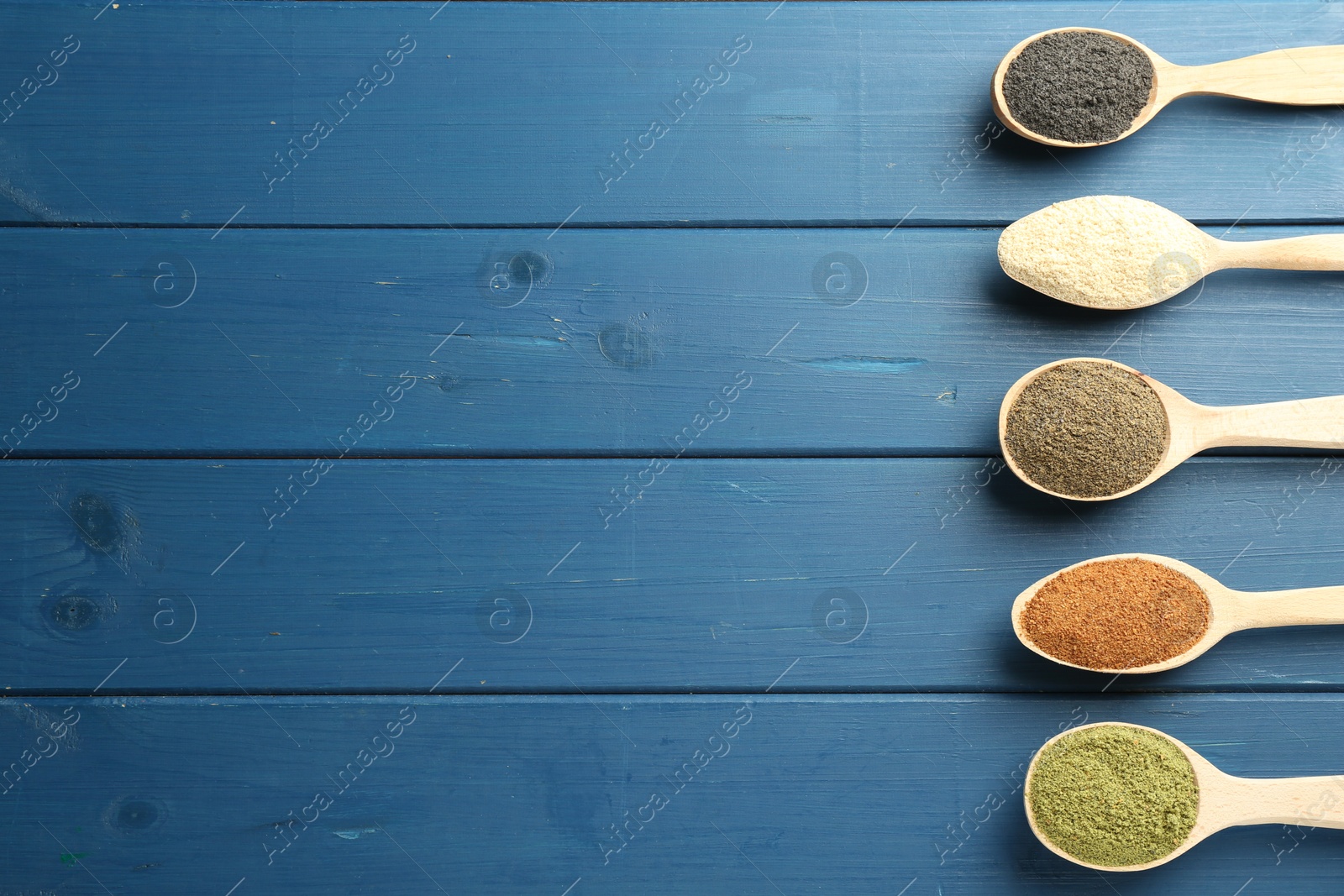 Photo of Different superfood powders in spoons on blue wooden table, flat lay. Space for text