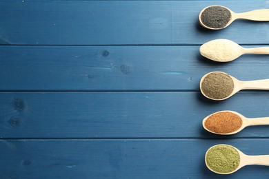 Photo of Different superfood powders in spoons on blue wooden table, flat lay. Space for text