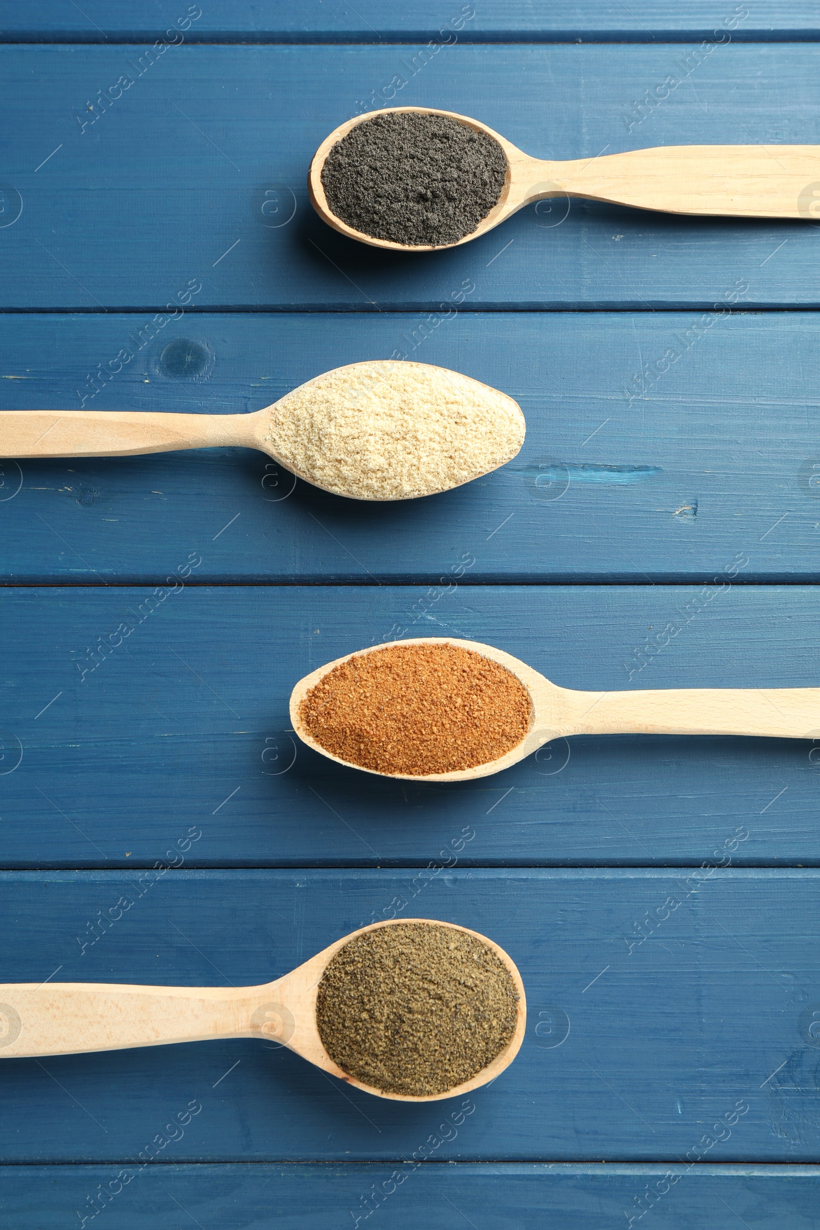 Photo of Different superfood powders in spoons on blue wooden table, flat lay