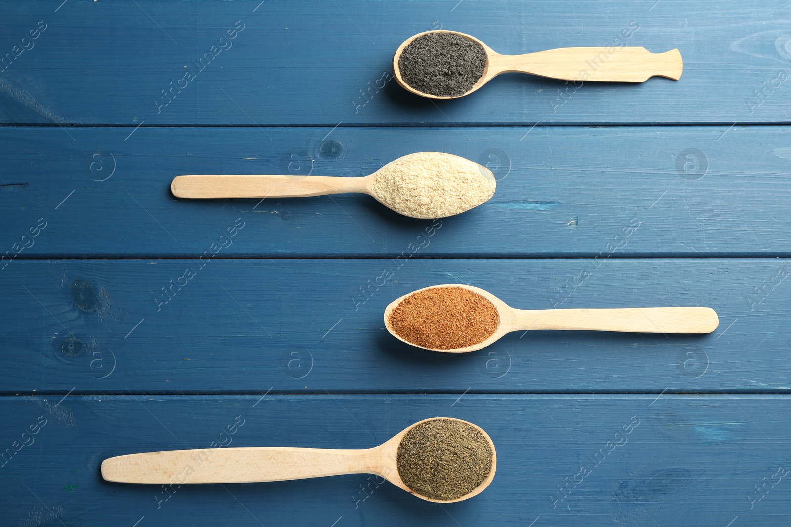 Photo of Different superfood powders in spoons on blue wooden table, flat lay