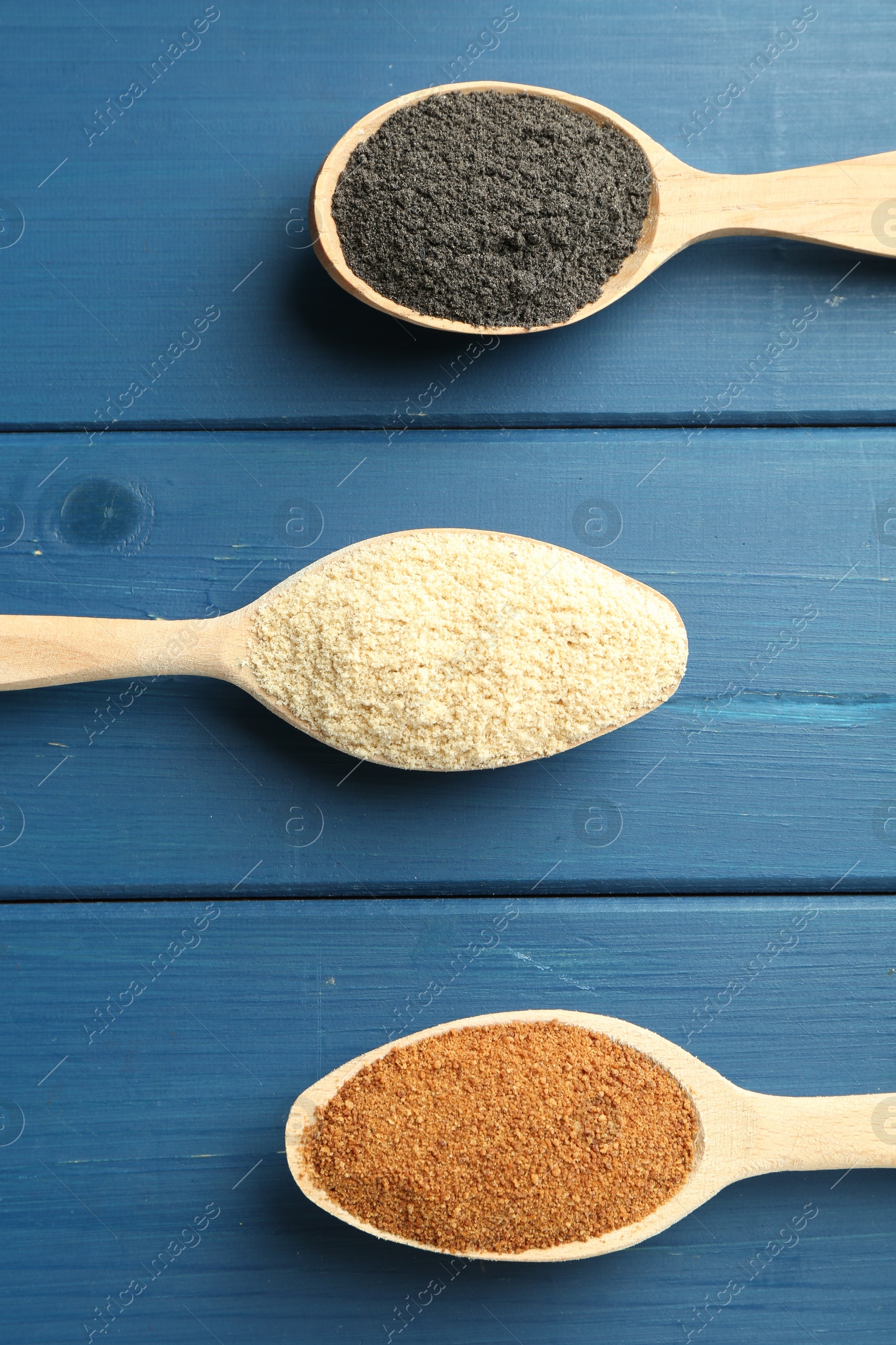 Photo of Different superfood powders in spoons on blue wooden table, flat lay