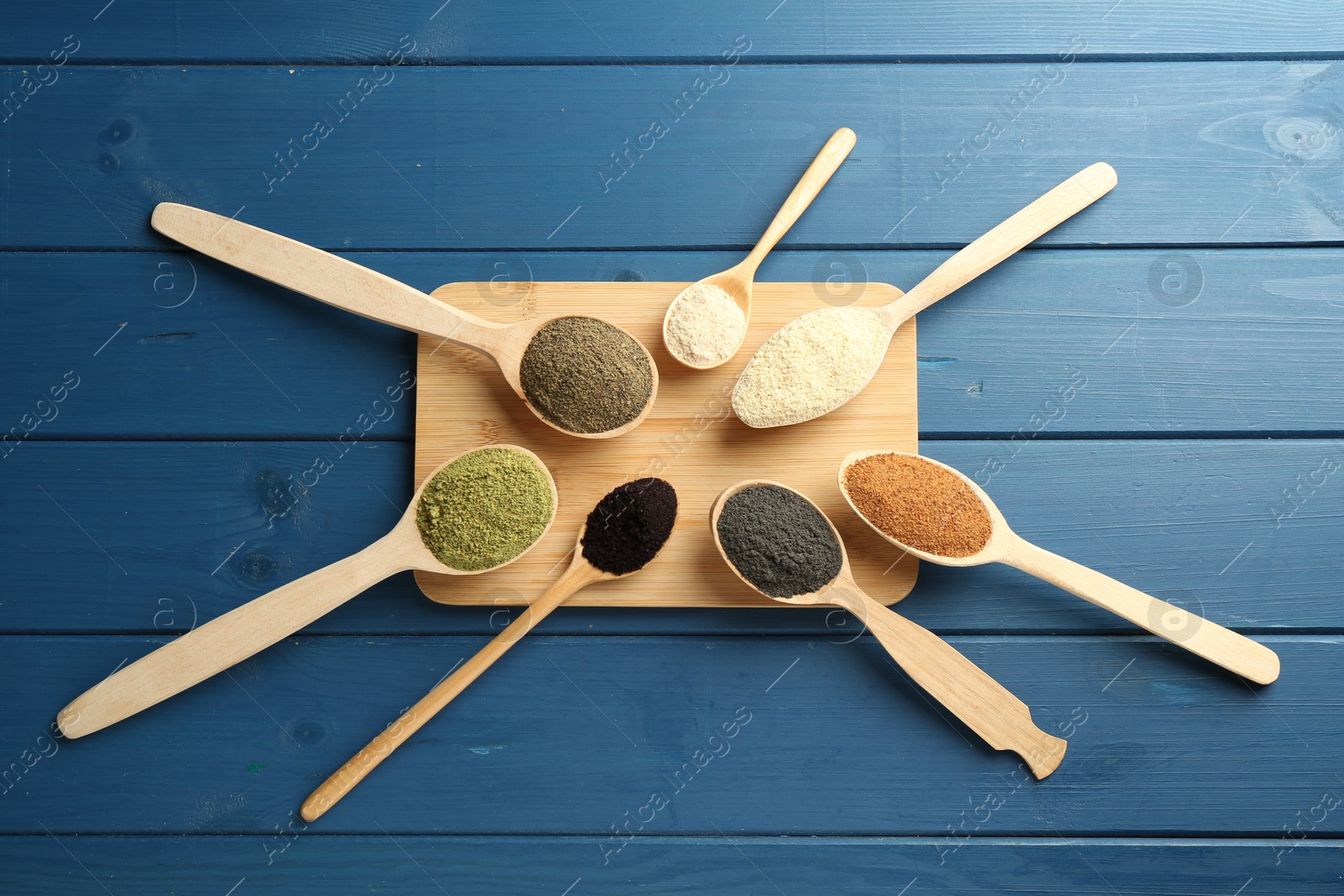 Photo of Different superfood powders in spoons on blue wooden table, top view