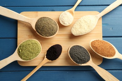 Photo of Different superfood powders in spoons on blue wooden table, top view