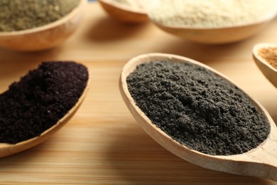 Photo of Different superfood powders in spoons on wooden table, closeup