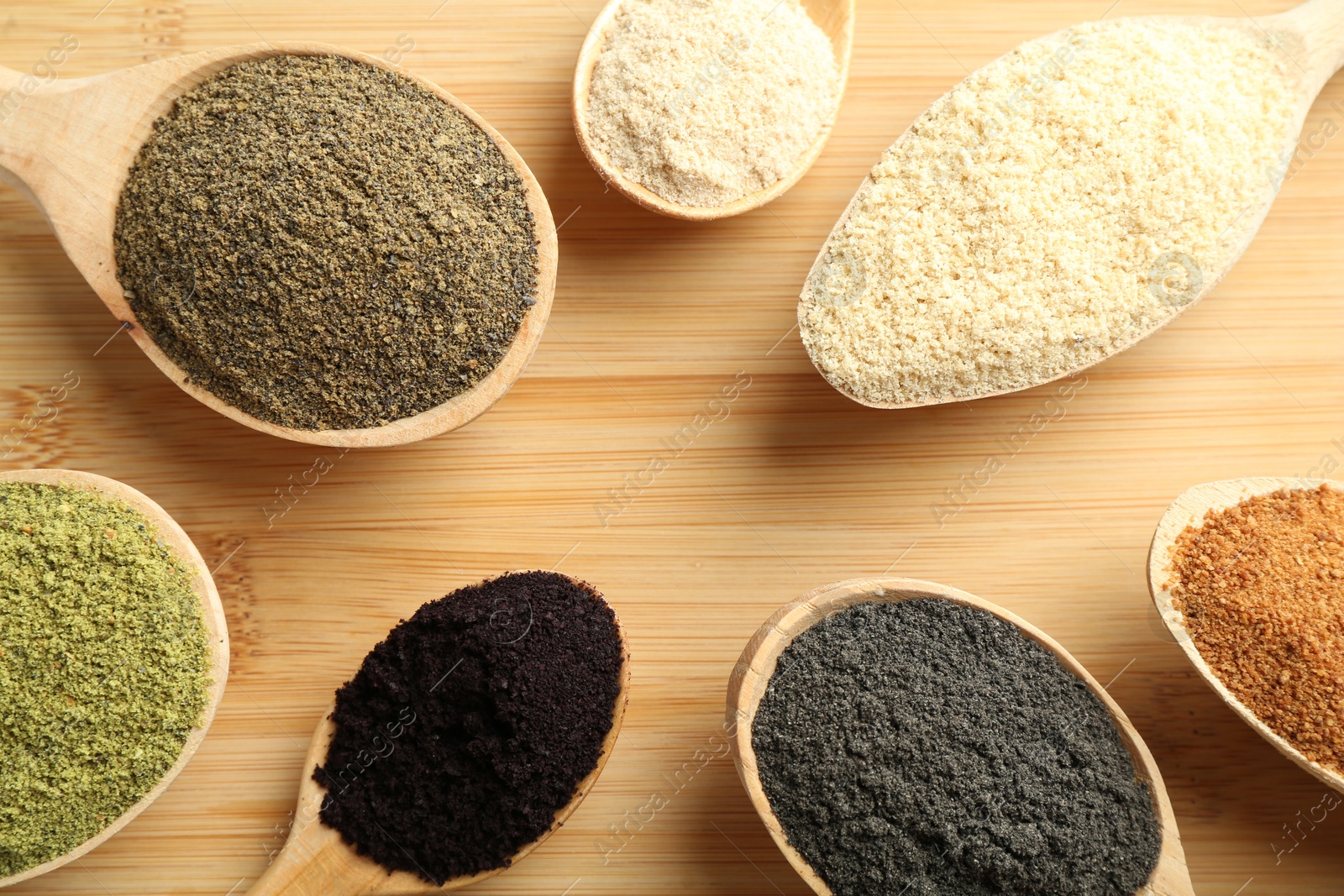 Photo of Different superfood powders in spoons on wooden table, flat lay