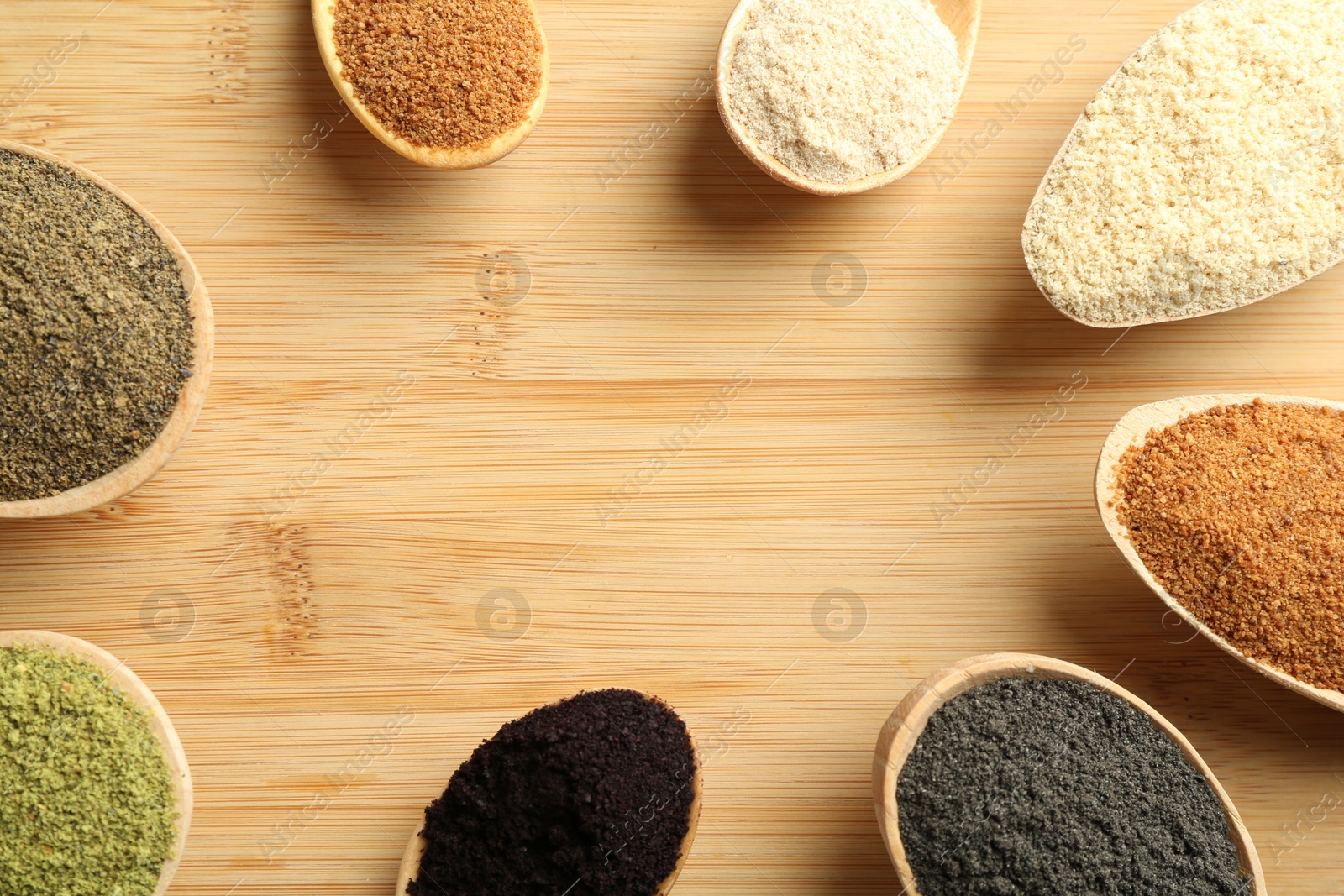 Photo of Different superfood powders in spoons on wooden table, flat lay. Space for text