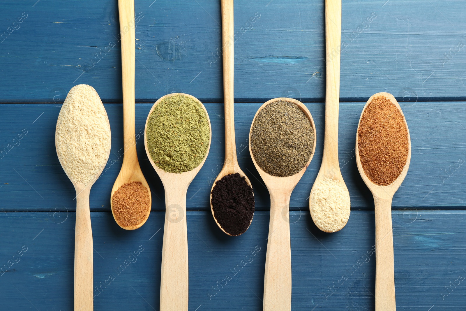 Photo of Different superfood powders in spoons on blue wooden table, flat lay