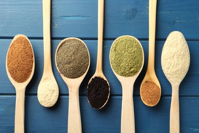 Photo of Different superfood powders in spoons on blue wooden table, flat lay