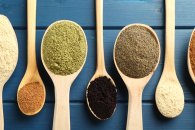 Photo of Different superfood powders in spoons on blue wooden table, flat lay