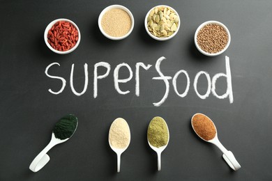 Photo of Word Superfood and different healthy powders on black table, flat lay