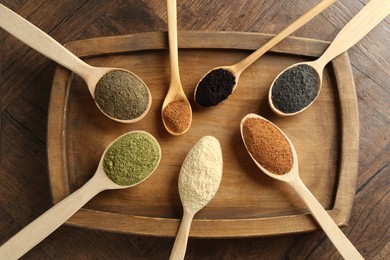 Photo of Different superfood powders in spoons on wooden table, top view