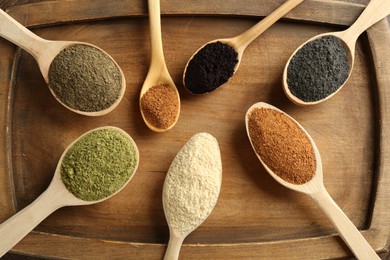 Photo of Different superfood powders in spoons on wooden board, top view